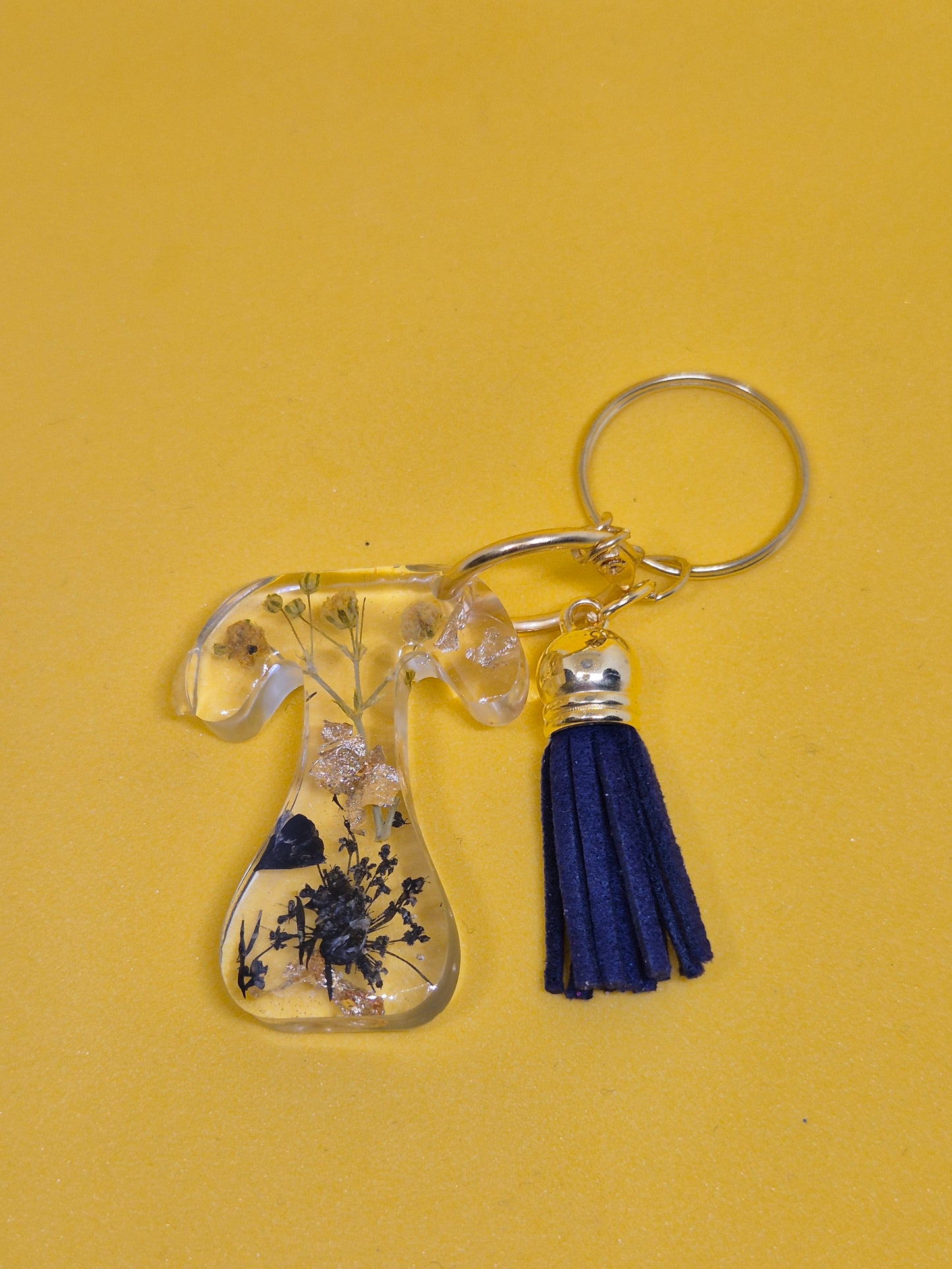 Llavero letra T de resina epoxi transparente con flores secas, pan de oro y borla azul