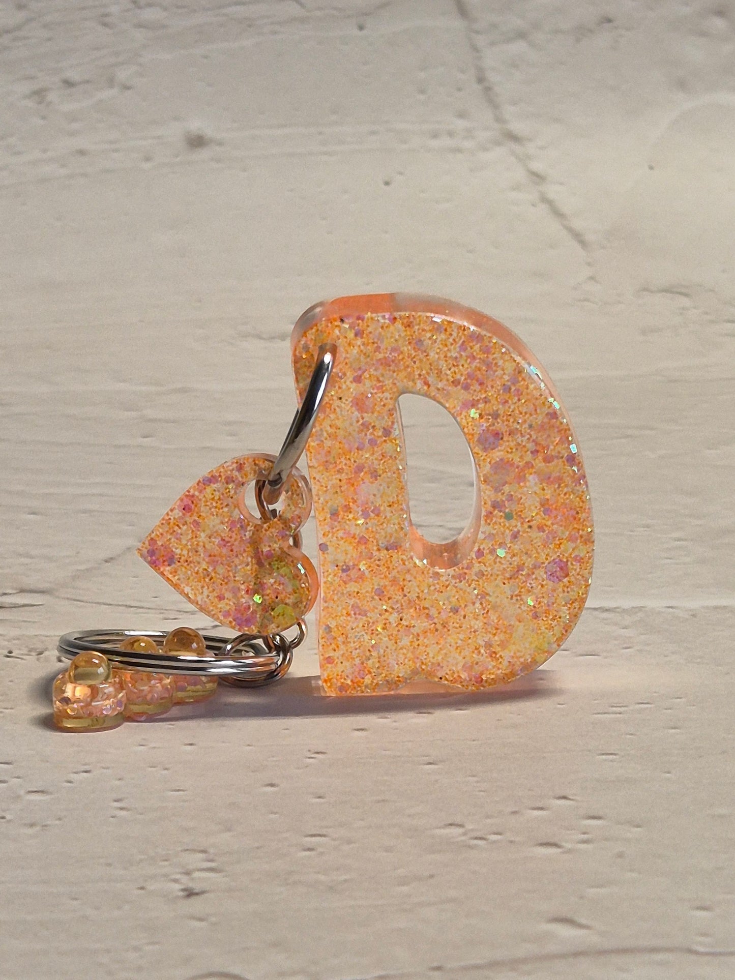 Llavero letra D de resina epoxi naranja con brillo holográfico, abalorios y detalle de corazón