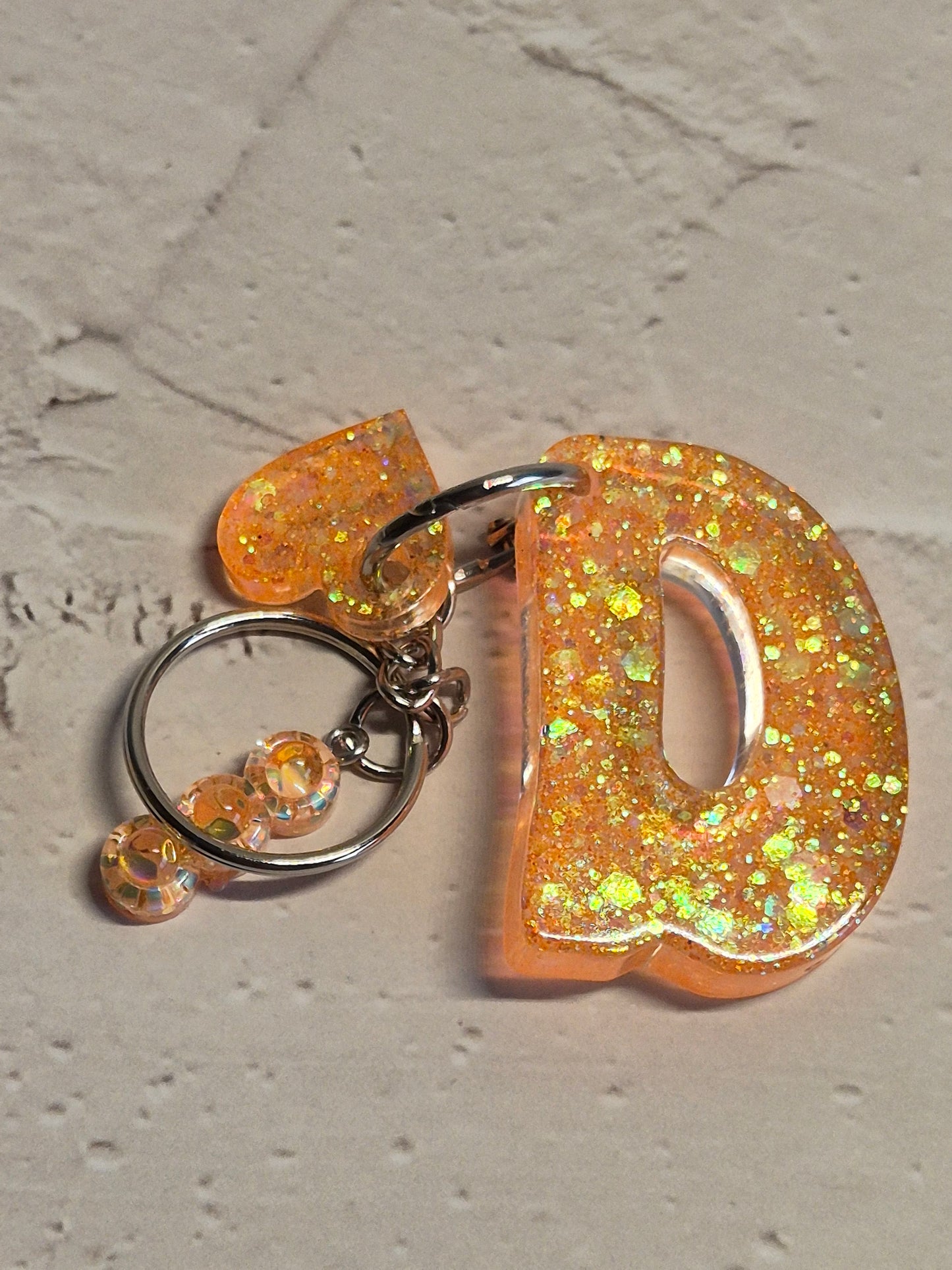 Llavero letra D de resina epoxi naranja con brillo holográfico, abalorios y detalle de corazón