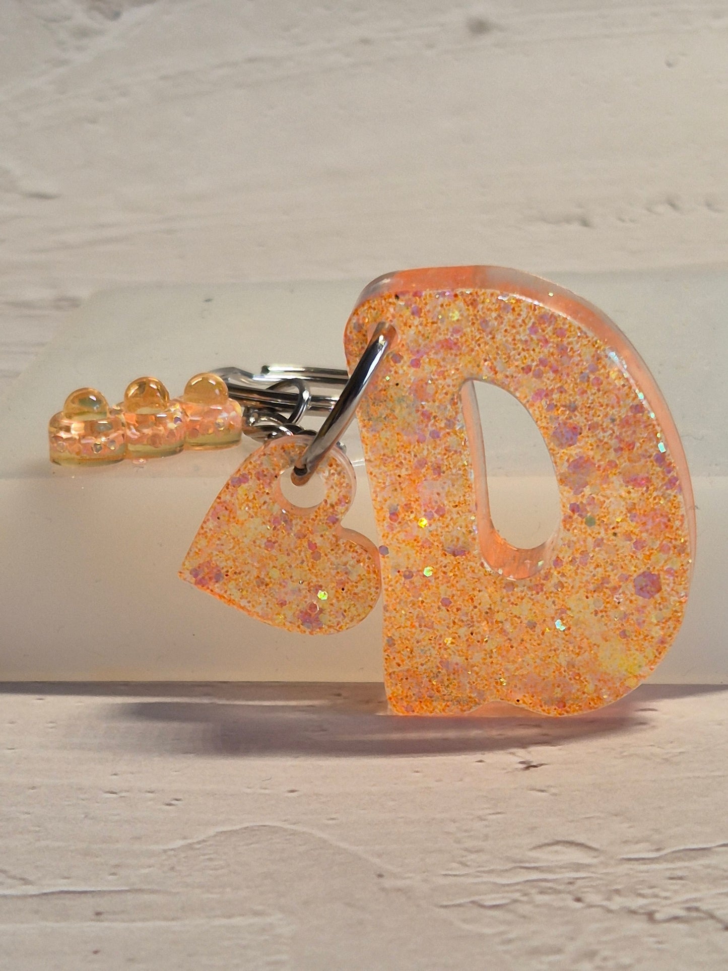 Llavero letra D de resina epoxi naranja con brillo holográfico, abalorios y detalle de corazón