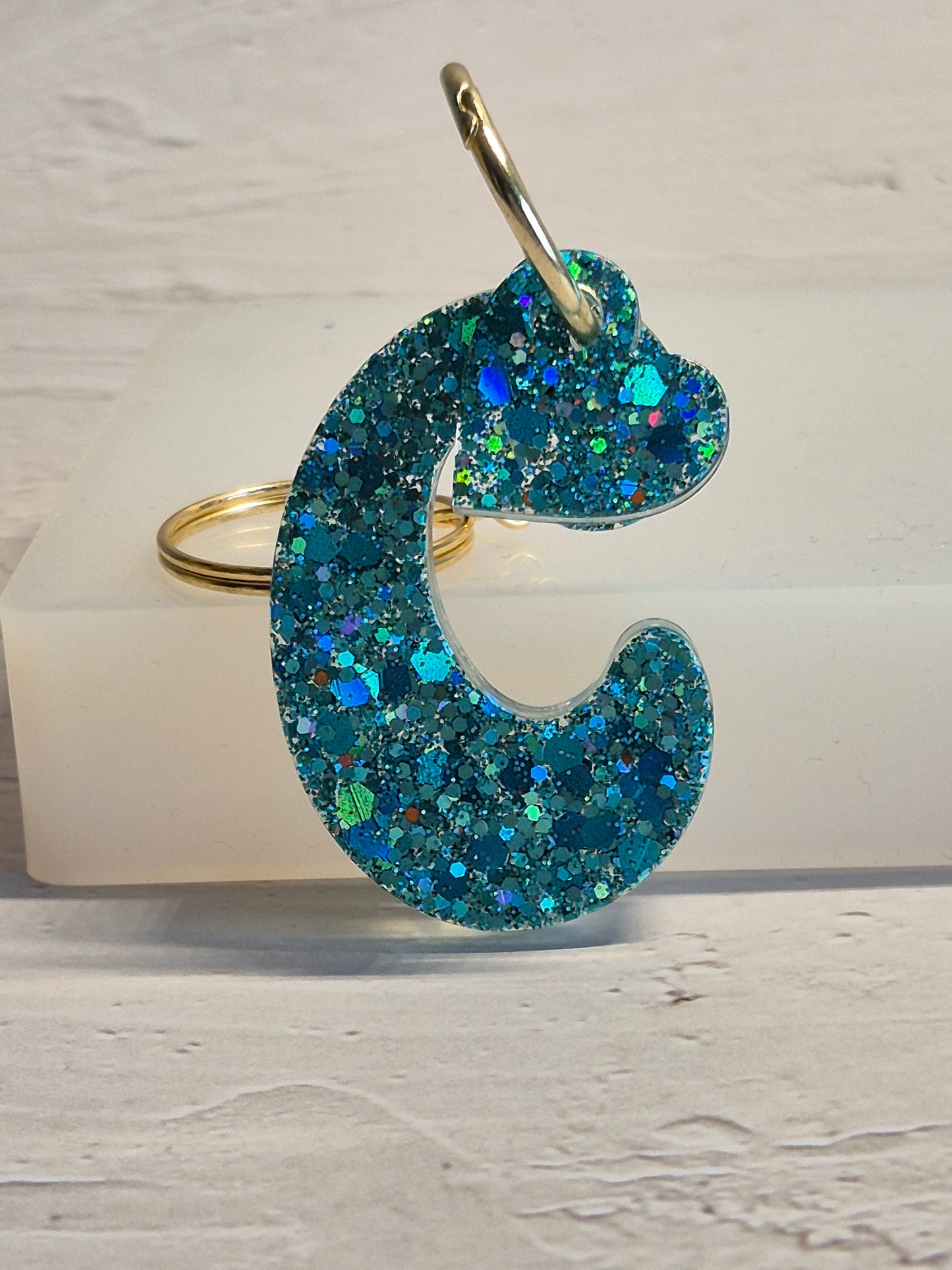 Llavero letra C de resina epoxi azul turquesa con brillo holográfico y detalle de corazón