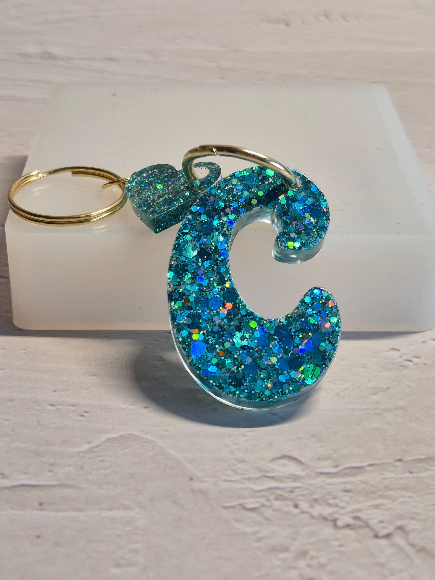Llavero letra C de resina epoxi azul turquesa con brillo holográfico y detalle de corazón