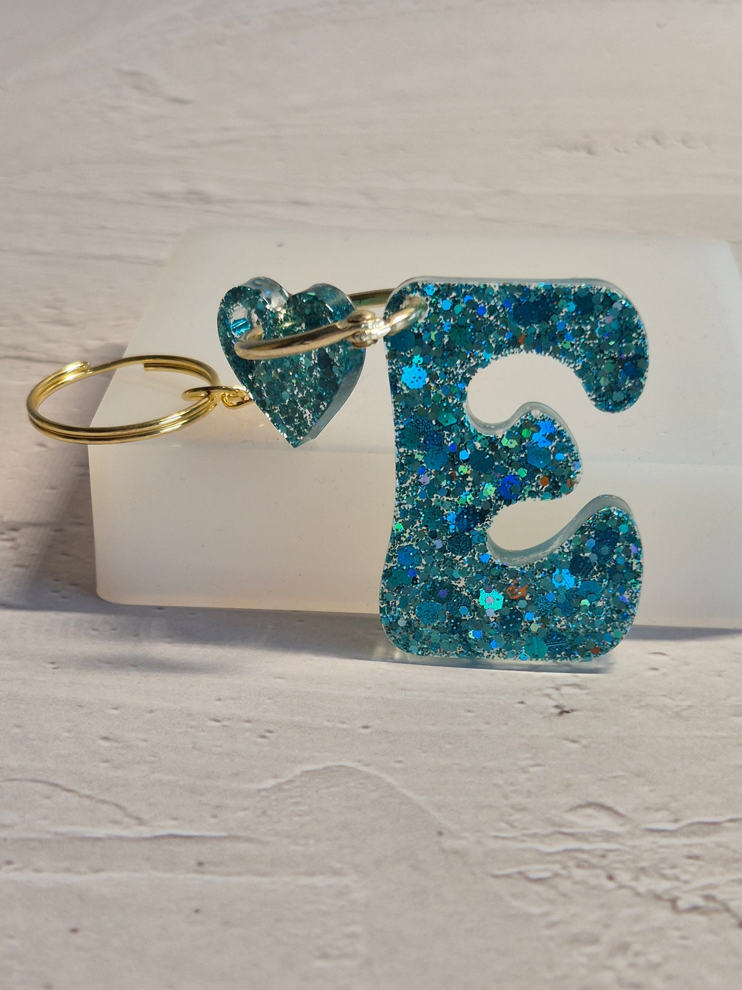 Llavero letra E de resina epoxi azul turquesa con brillo holográfico y detalle de corazón