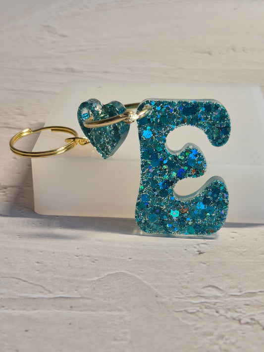 Llavero letra E de resina epoxi azul turquesa con brillo holográfico y detalle de corazón