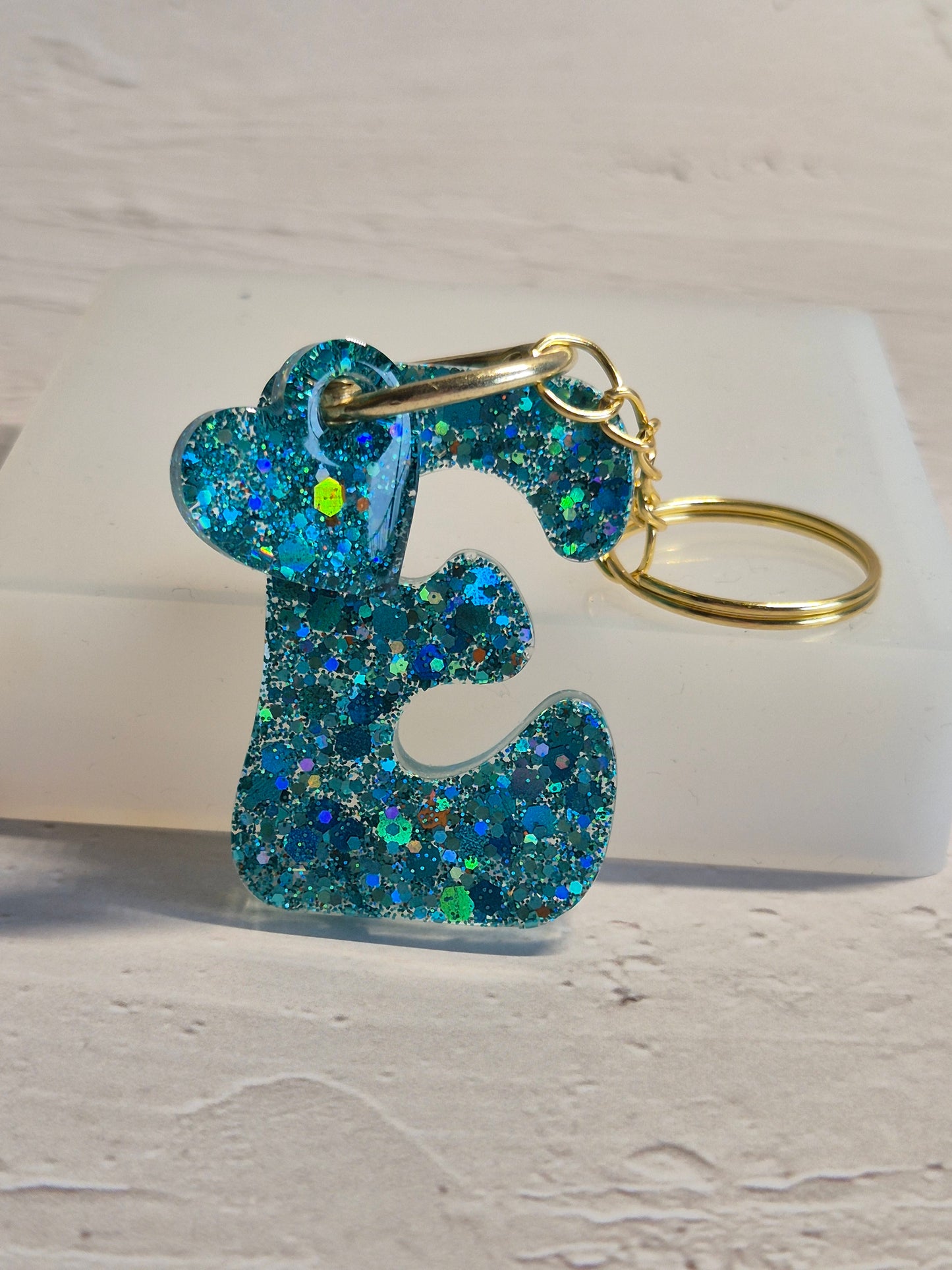 Llavero letra E de resina epoxi azul turquesa con brillo holográfico y detalle de corazón