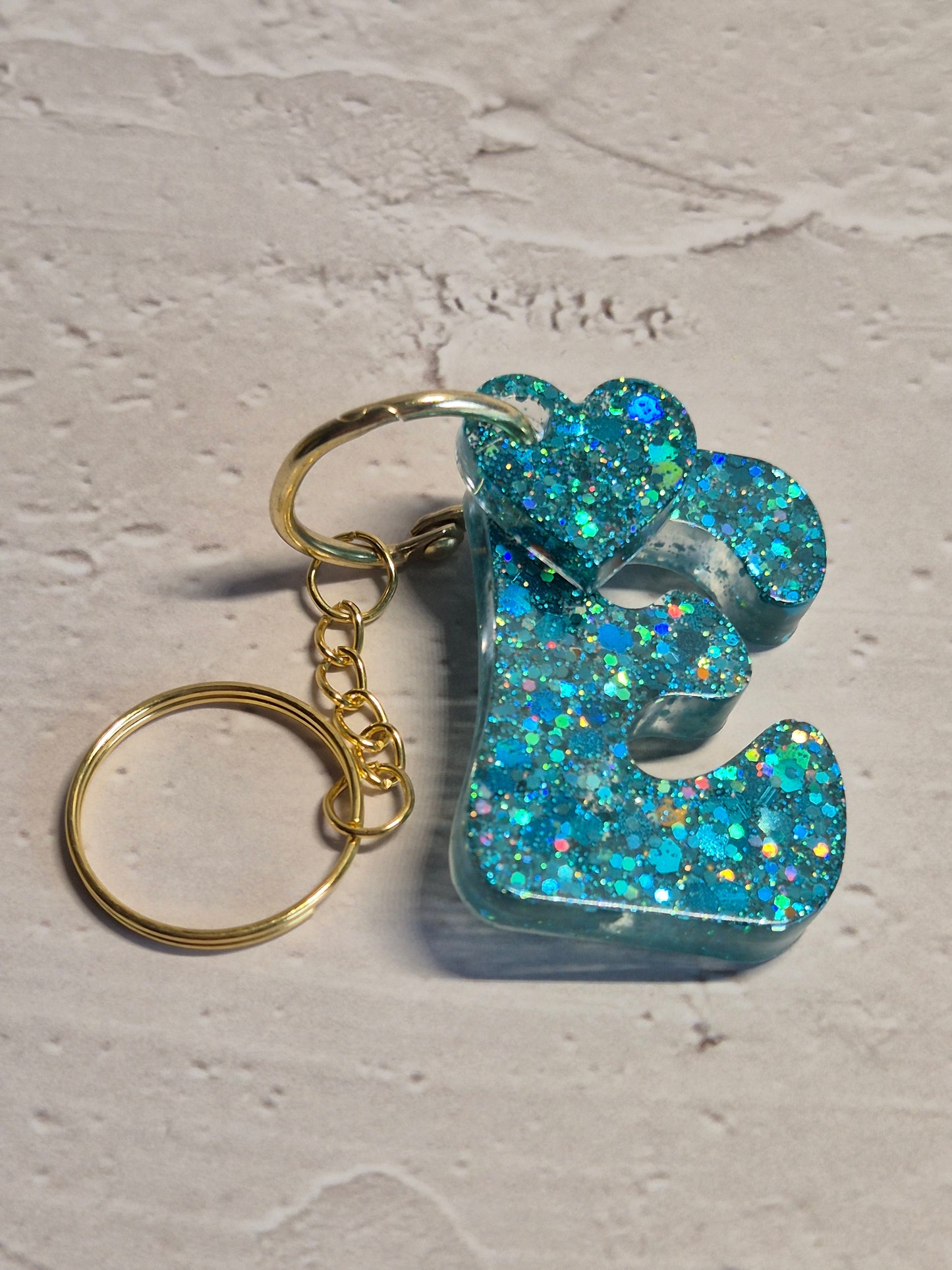Llavero letra E de resina epoxi azul turquesa con brillo holográfico y detalle de corazón