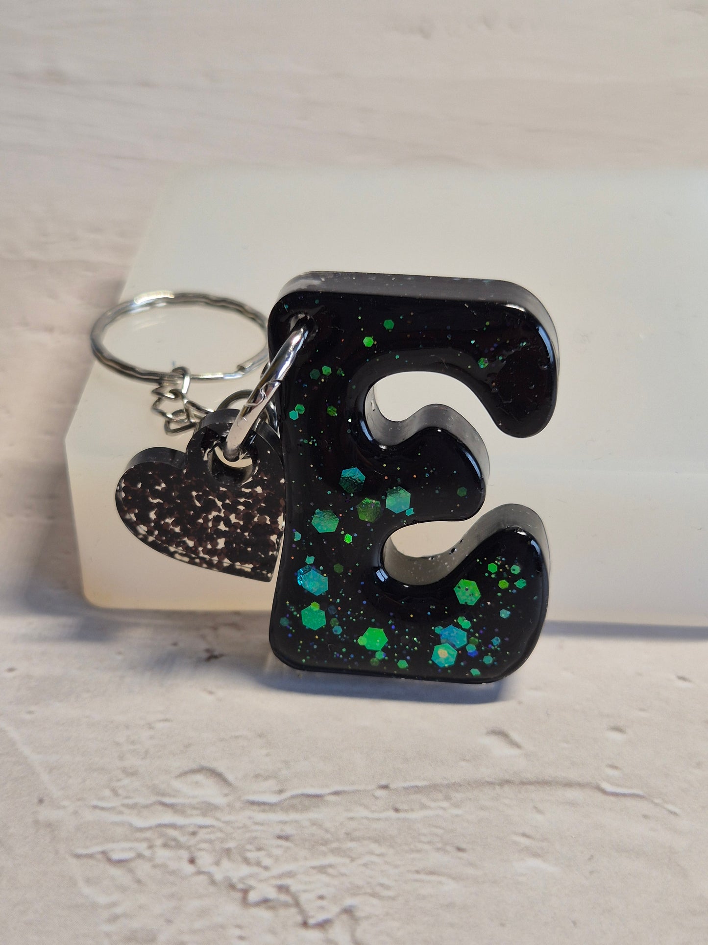 Llavero letra E de resina epoxi negra con brillo verde holográfico y corazón