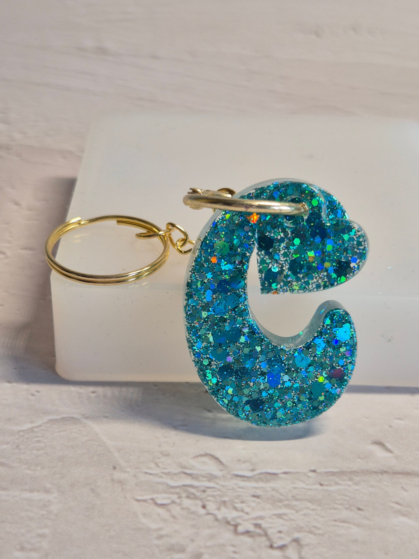 Llavero letra C de resina epoxi azul turquesa con brillo holográfico