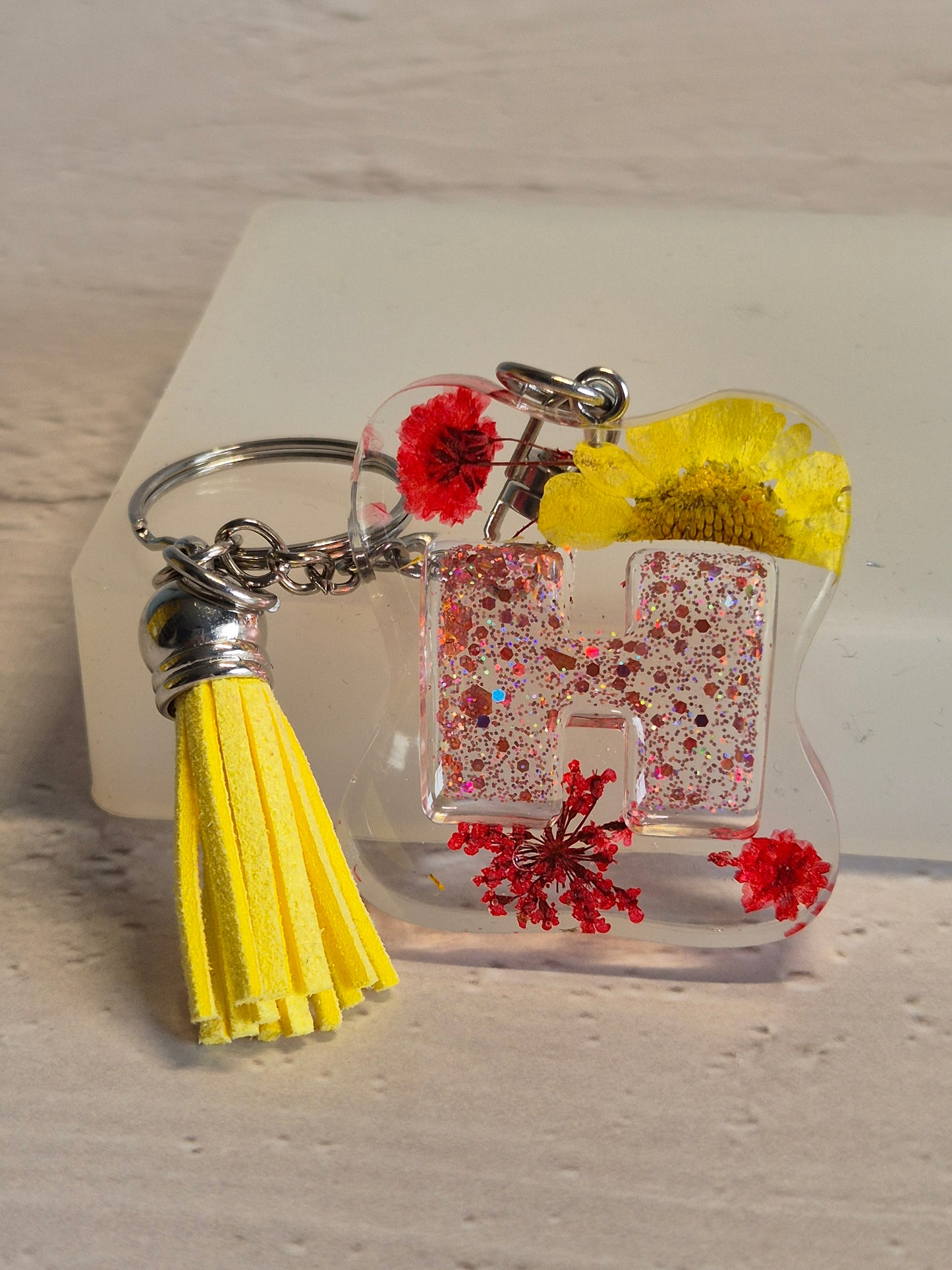 Llavero letra H de resina epoxi fucsia transparente con flores secas, pan de oro y borla fucsia
