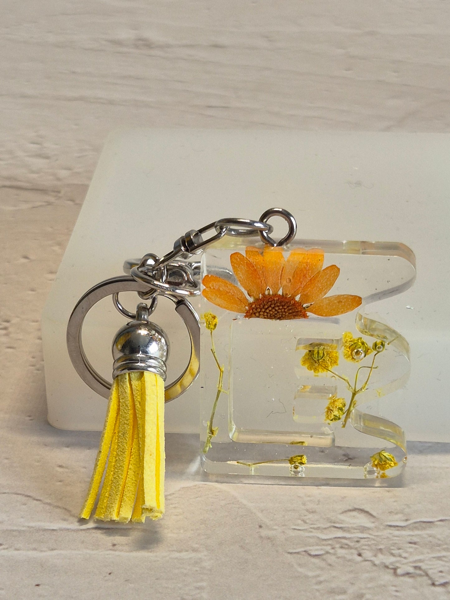 Llavero letra E de resina epoxi transparente con flores secas y borla amarilla