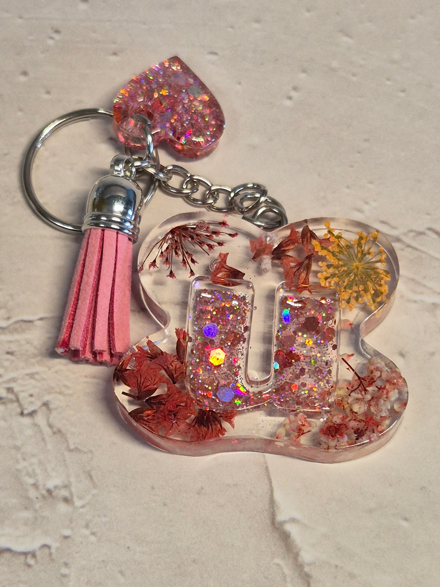Llavero letra U de resina epoxi transparente con flores secas, glitter y borla rosa